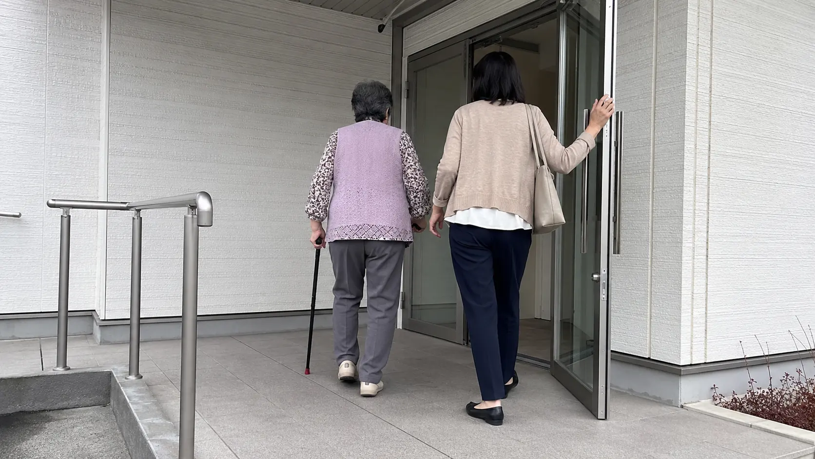 杖をついたご年配のお客様に付き添って建物の入口へ向かう支援スタッフ